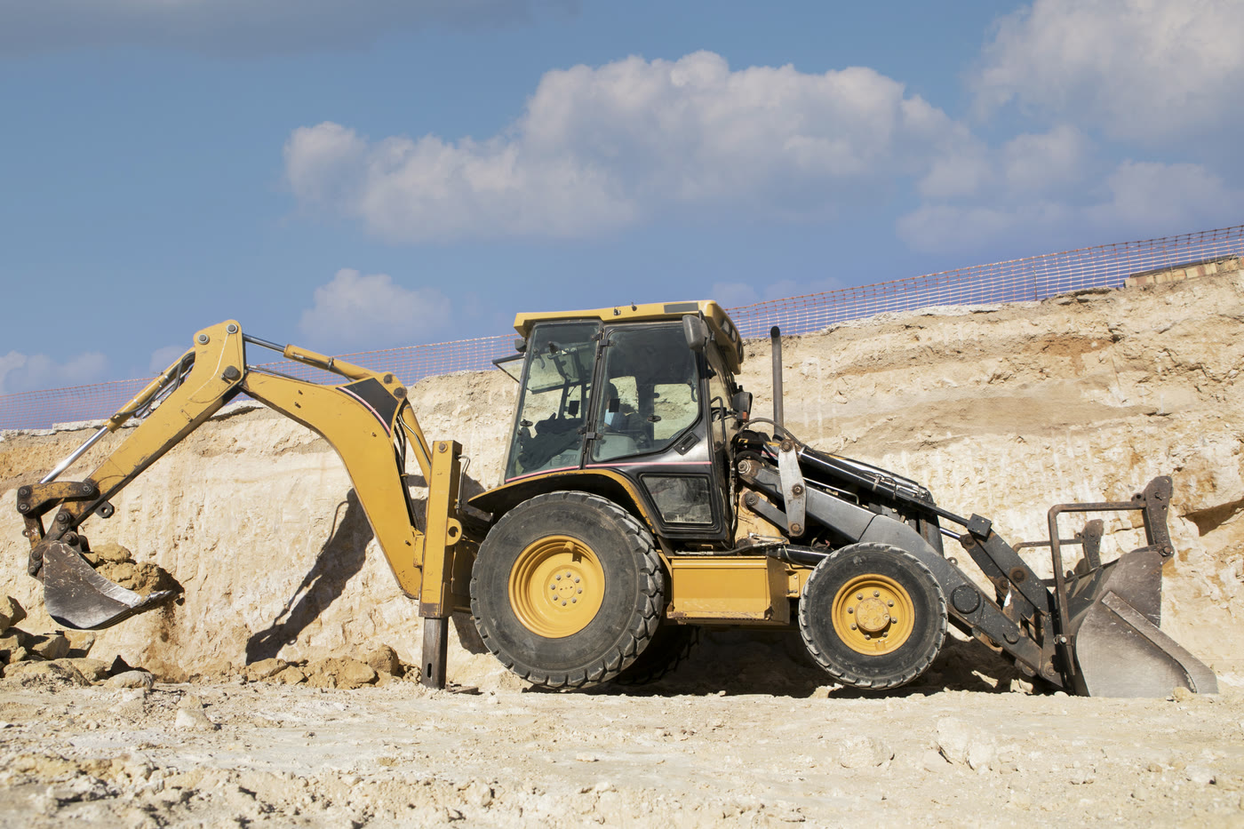 Vertex backhoe loader dumping fill dirt under a blue sky